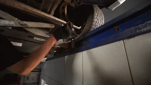 Mechanic stands in the pit and checks suspension at the car service station Stock Footage 110996942