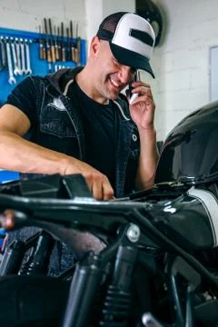 Mechanic talking phone while fixing motorbike Stock Photos