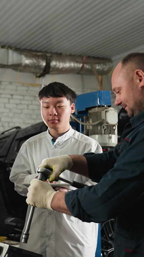 Mechanic Teaching Students How to Loosen a Bolt in Automotive Workshop Stock Footage 318226892