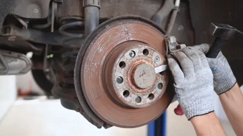 A mechanic uses a hammer and a chisel to unscrew the old brake disc on the wheel Video stock 161259851