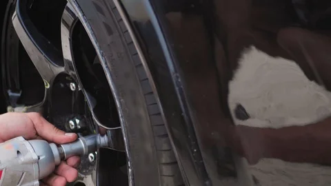 Mechanic uses a pneumatic tool to fasten black 6-spoke wheel to black fancy car 스톡 동영상 128492790