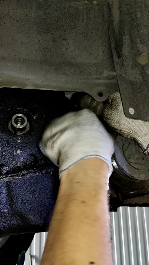 A mechanic uses a ratchet wrench under an oily engine pan. Stock Footage 338364751