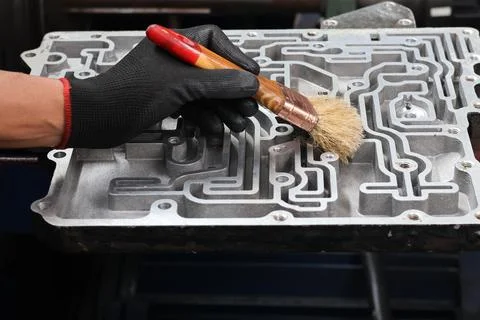 Mechanic using a brush on an automatic transmission valve body. Stock Photos