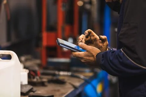 Mechanic using cell phone in the workshop. Hands full of grease. Technology c Stock Photos