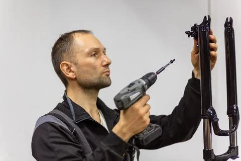 Mechanic using a cordless drill to assemble black bicycle fork parts Stock Photos
