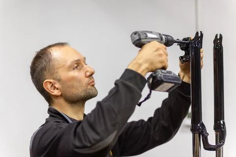 Mechanic using a cordless drill to assemble black bicycle fork parts Stock Photos