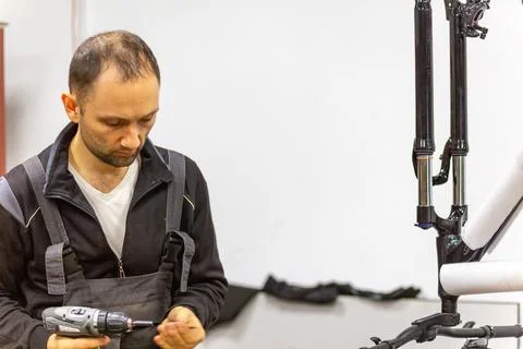 Mechanic using a cordless drill to assemble black bicycle fork parts Stock Photos