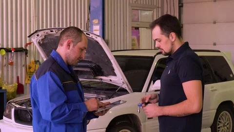 Mechanic using a digital tablet while doing test on a car in a garage Stock Footage 75683759