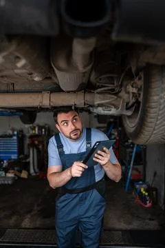 Mechanic using a digital tablet while inspecting a car from below in a repair Stock Photos