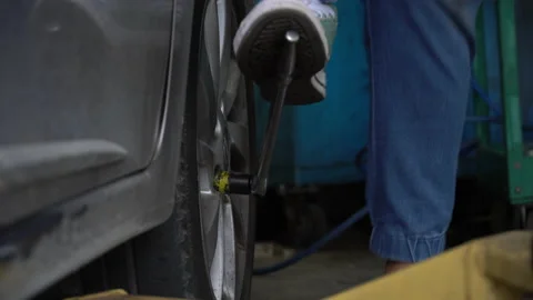 Mechanic using foot with wheel wrench remove and changing wheel on car in wor Stock Footage 147368081