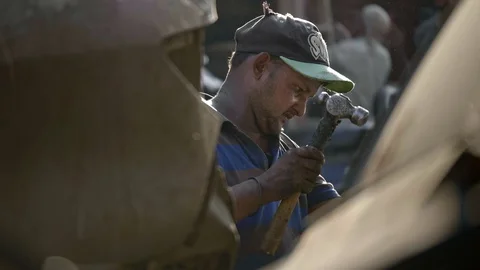 A mechanic using hammer to dismantle an old car/ vehicle in Chor Bazaar Stock Footage 128733347