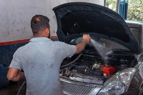 A mechanic is using a high-pressure hose to wash the engine of a car Stock Photos
