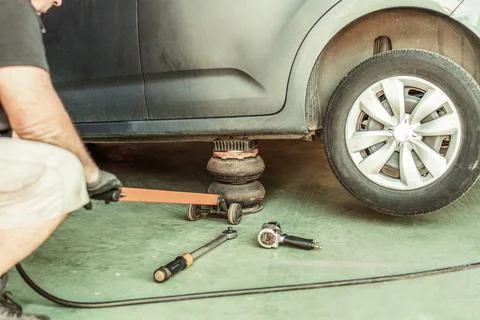 Mechanic using a pneumatic jack under a car to lift it into a garage Stock Photos