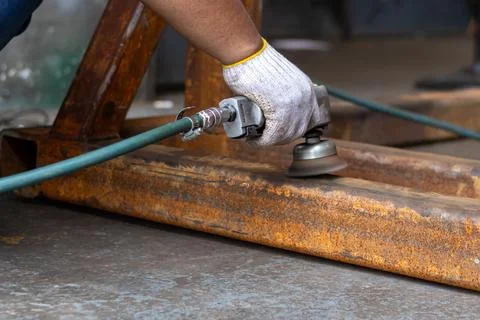 Mechanic using pneumatic wire cup brush to clean rusty steel frame. Foto stock