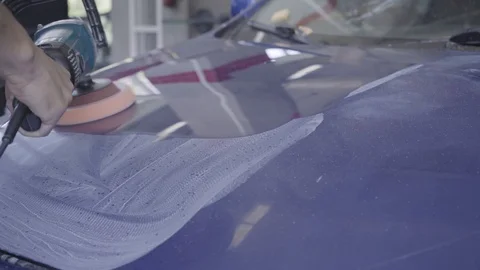 Mechanic using a rotary polisher on a the paintwork of a blue car in a body shop Vídeo Stock 95557077