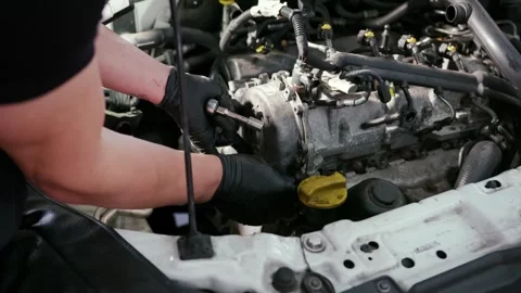 Mechanic using screwdriver on car engine components inside open engine bay Stock Footage 340875725