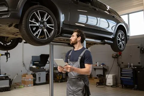 Mechanic using tablet inspecting car on lift in garage 스톡 사진