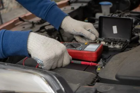 Mechanic using voltmeter checking voltage of car battery in car service centr Foto stock