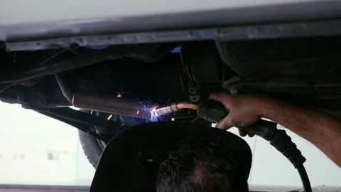 Mechanic welding under car chassis with sparks flying in auto workshop Stock Footage 337777654