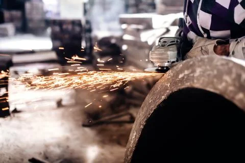 Mechanic worker using grinder for polishing an iron block Stock Photos