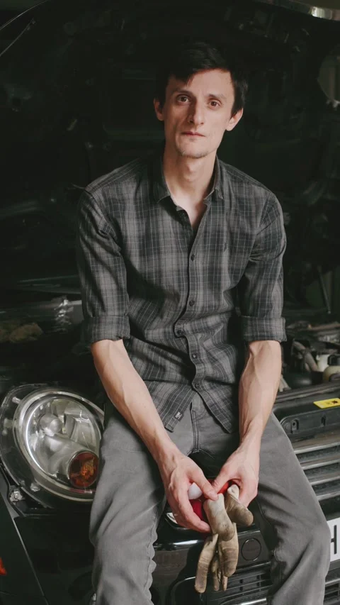 Mechanic working on a car in a dimly lit garage, taking a break while holding Stock-Footage 303810135