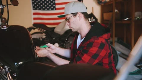 Mechanic working on a motorcycle in a garage while an American flag hangs in the Stock Footage 313846312