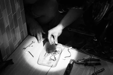 Mechanic Working Under Spotlight Sorting Parts Black and White Foto stock