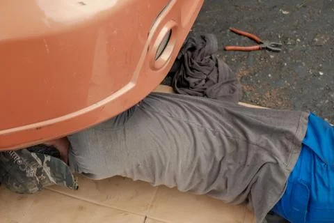 Mechanic in working uniform lying down and working under car at auto service  Stock Photos
