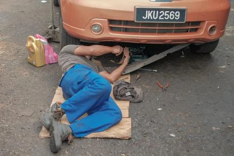Mechanic in working uniform lying down and working under car at auto service  Stock Photos