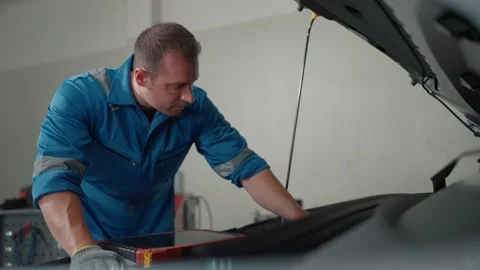 Mechanic works under open EV car hood Stock Footage 338332496