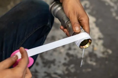 Mechanic wraps white thread seal tape around metal pipe fitting in industri.. Stock Photos