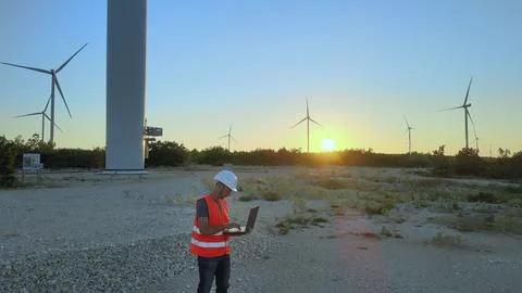 Mechanical engineer adjusting wind turbine settings from his laptop at sunset. Foto stock