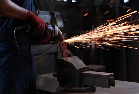 Mechanical engineer operating angle grinder cutter in dark metal workshop with Stock Photos