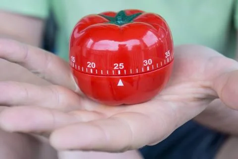 Mechanical red tomato kitchen timer set to 25, held by one open hand Stock-Fotos