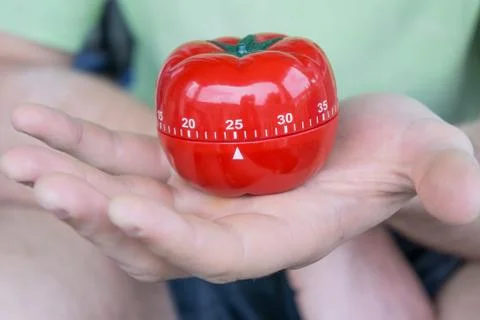 Mechanical red tomato kitchen timer set to 25, held by one open hand Stock Photos