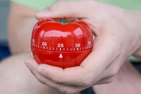 Mechanical red tomato kitchen timer set to 25 minutes , gripped by one hand Stock Photos