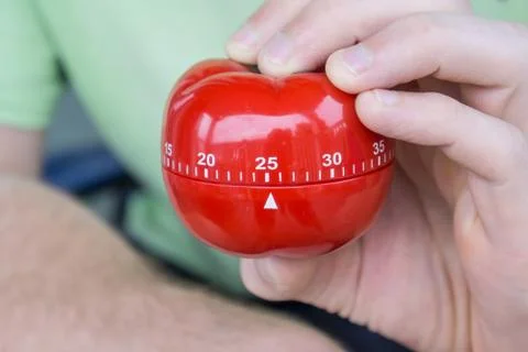 Mechanical red tomato kitchen timer set to 25 minutes , gripped by one hand Stock Photos