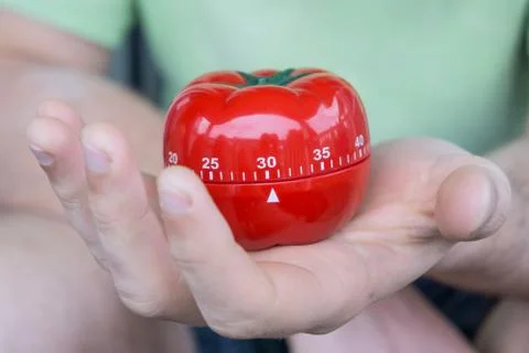 Mechanical red tomato kitchen timer set to 30, held by one open hand Stock Photos