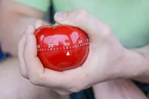 Mechanical red tomato kitchen timer set to 30 minutes , gripped by one hand Stock Photos