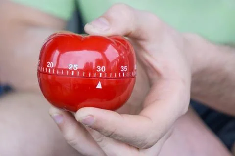 Mechanical red tomato kitchen timer set to 30 minutes , gripped by one hand Stock Photos