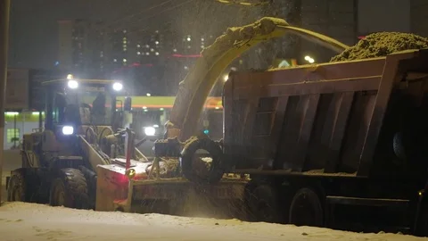 Mechanical screw type plow truck cleans road into tipper truck after snow fall Stock Footage