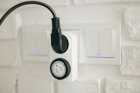 Mechanical Timer Socket Plugged Into Wall Outlet Beside Light Switches. Modern Stock Photos