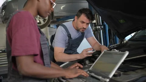 Mechanics diagnosing car problems using laptop in auto repair shop Stock Footage 316484797
