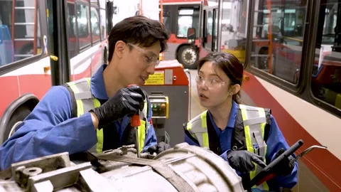 Mechanics with digital tablet fixing bus engine in transit garage Stock Footage 221035363