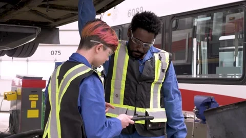 Mechanics with digital tablet talking in bus maintenance facility Stock Footage 221035968