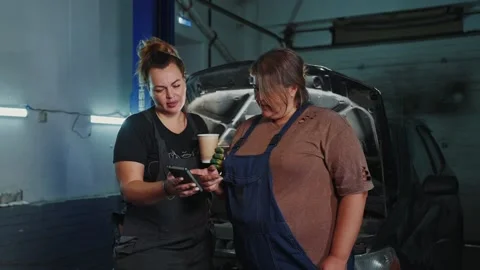 Mechanics discuss repairs while enjoying coffee in their workshop Stock Footage 294973954