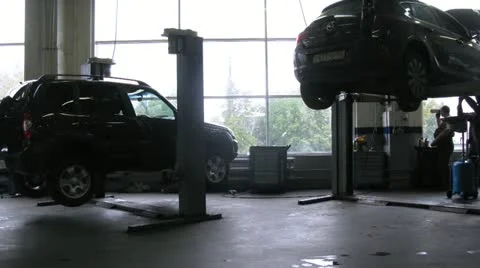 Mechanics elevate cars on lifting-jack hoist in garage Stock Footage 12368130