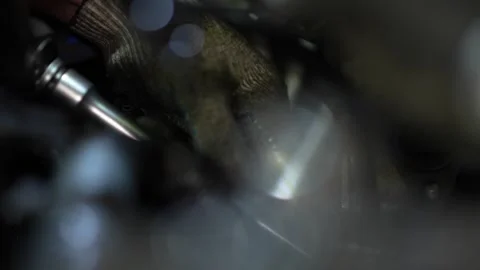 A mechanic's gloved hand works deep inside a dark engine bay, partially obscu Stock Footage 345109411