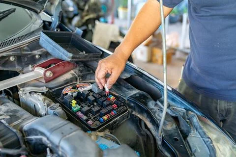 A mechanic's hand inserting a small red blade fuse into a car's fuse box l Stock-Fotos