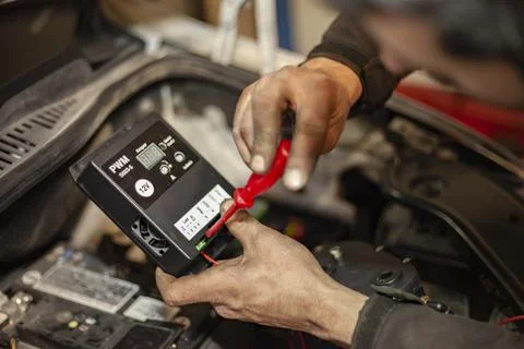 Mechanic's hands adjust the hydrogen system control unit in the car engine Stock Photos